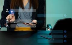 Mulher interage com uma interface digital holográfica via tablet, representando tecnologia de gestão de contatos ou atendimento ao cliente.