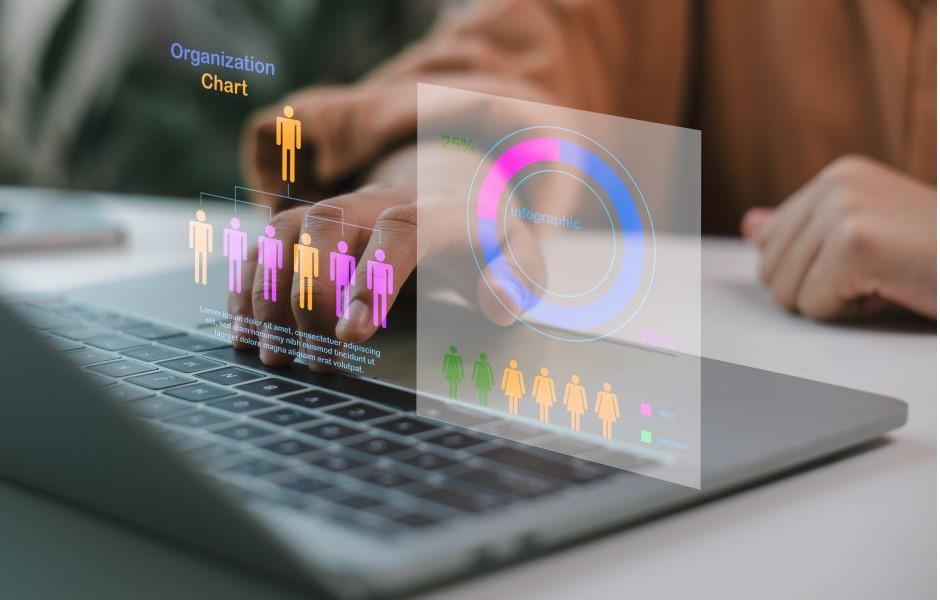 Mãos sobre notebook com projeção holográfica de organograma e infográficos, representando gestão de pessoas e estrutura organizacional.