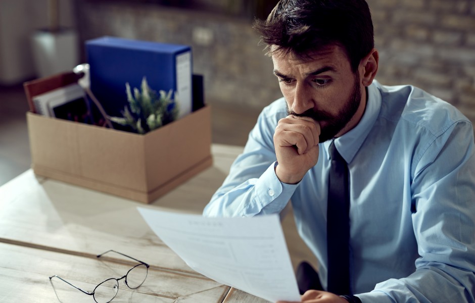  Um homem com expressão preocupada observa um documento enquanto morde a mão, aparentando ansiedade.