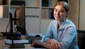 Jovem profissional sorrindo sentada à frente do computador em um escritório.