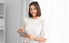 Mulher sorridente segurando um tablet em ambiente bem iluminado e moderno, transmitindo alegria e satisfação ao usar tecnologia.