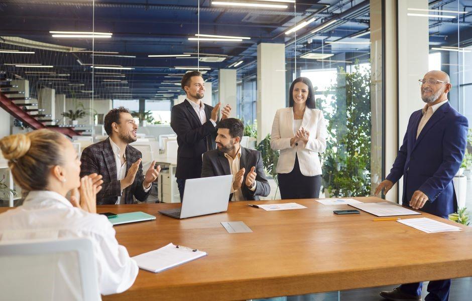 Equipe corporativa aplaude em sala de reunião moderna, celebrando um resultado ou reconhecendo um colega.