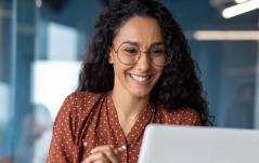 Mulher sorridente usando óculos enquanto olha para o notebook, demonstrando entusiasmo e engajamento no trabalho.