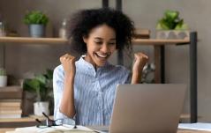 Mulher comemorando animada na frente do notebook, com punhos erguidos em sinal de vitória.