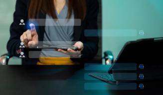 Profissional em escritório usando um tablet com interface de recrutamento/contatos sobreposta, com laptop aberto na mesa ao lado.