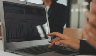 Pessoa analisando gráficos de desempenho em um notebook durante uma reunião.