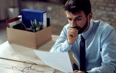  Um homem com expressão preocupada observa um documento enquanto morde a mão, aparentando ansiedade.
