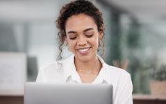 Mulher sorrindo enquanto trabalha no computador, transmitindo foco e satisfação em um ambiente profissional.