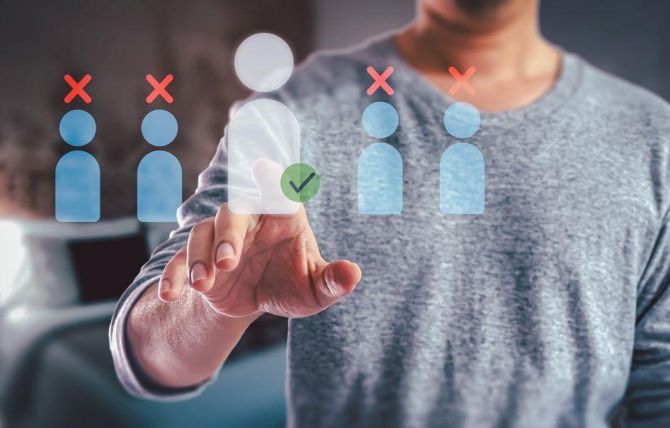 Mão selecionando um ícone de pessoa com check verde entre outros marcados com X, simbolizando seleção ou recrutamento de candidatos.
