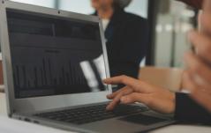 Pessoa analisando gráficos de desempenho em um notebook durante uma reunião.