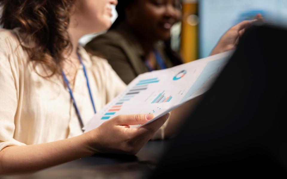 Duas mulheres em ambiente corporativo analisam juntas um relatório com gráficos coloridos.