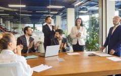 Equipe corporativa aplaude em sala de reunião moderna, celebrando um resultado ou reconhecendo um colega.
