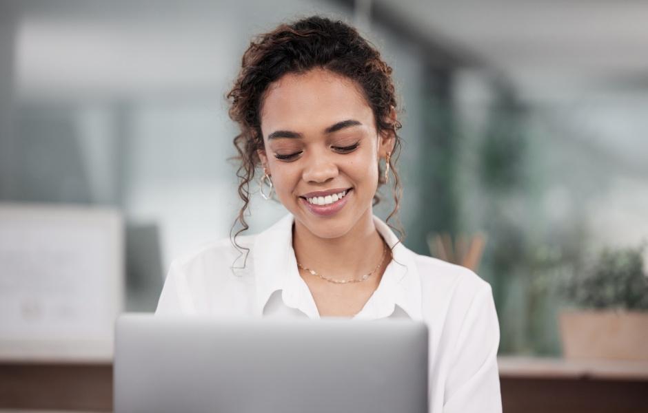 Mulher sorrindo enquanto trabalha no computador, transmitindo foco e satisfação em um ambiente profissional.